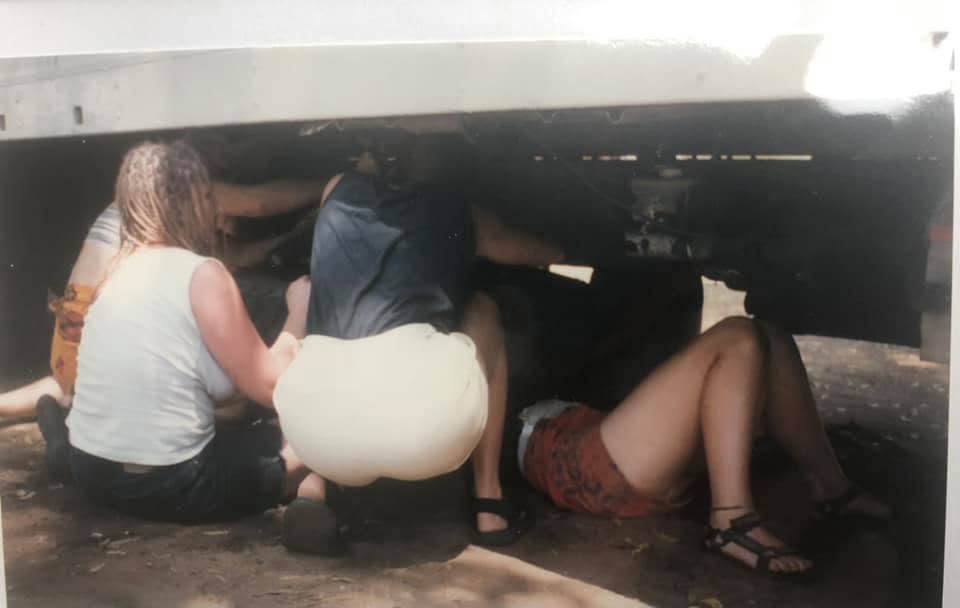 A group of people working together under a vehicle, with only their upper bodies and legs visible, engaged in maintenance or repair activities.