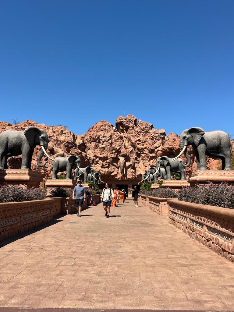A pathway leading towards a stone structure flanked by large elephant statues, set against a clear blue sky.