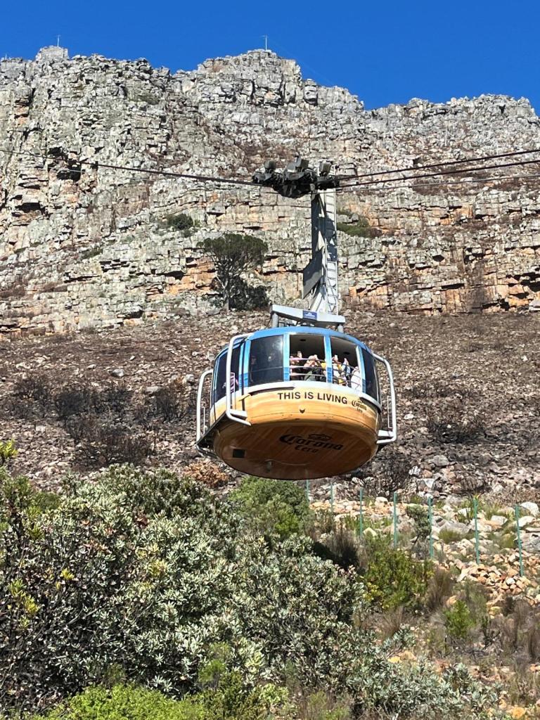A cable car with passengers ascends towards rocky terrain under a clear blue sky.