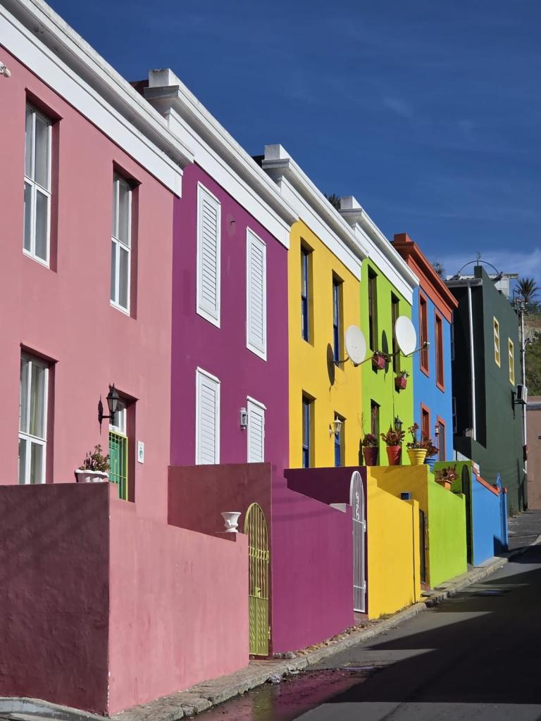 Colorful houses with pink, purple, yellow, and green facades along a street on a sunny day.
