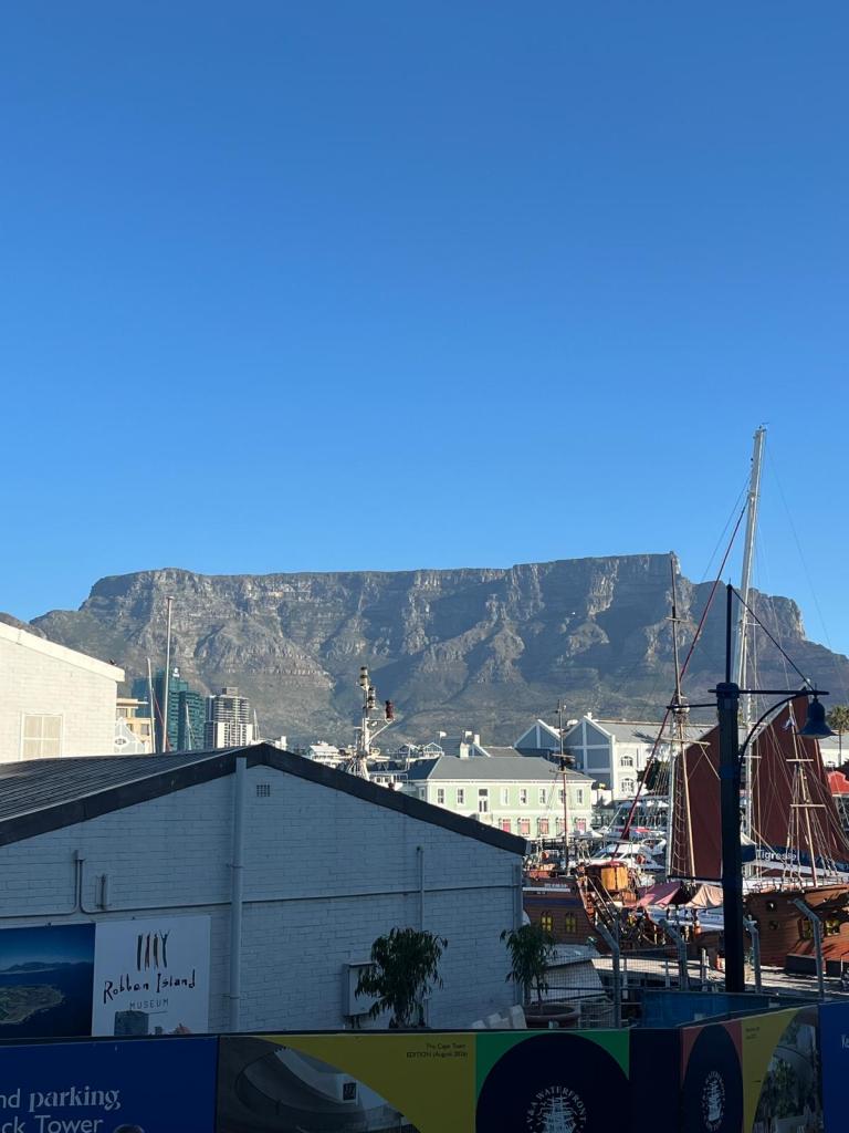View of Table Mountain in Cape Town against a clear blue sky, with harbor buildings and boats in the foreground.