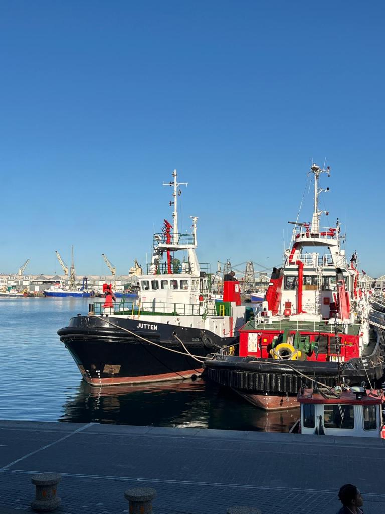 Two tugboats docked at a harbor under a clear blue sky.