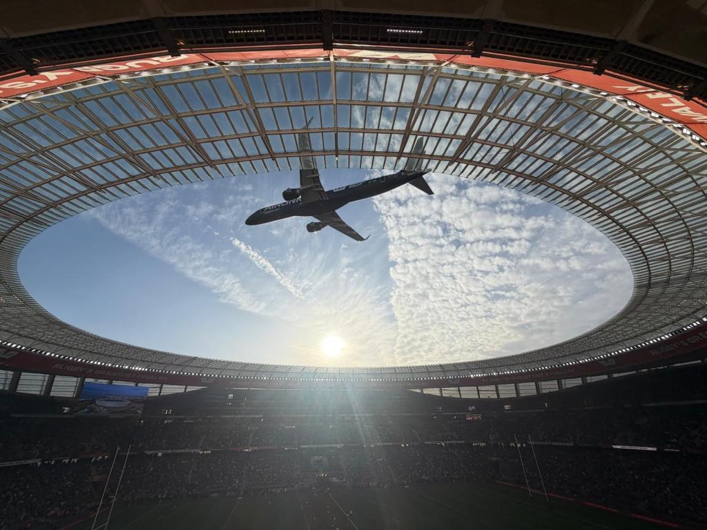 An airplane flying above a stadium with a clear sky and the sun setting in the background.