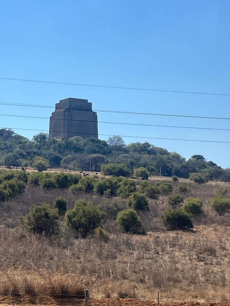 A large concrete monument atop a hill, surrounded by green and dry vegetation under a clear blue sky.